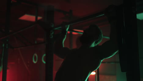 Two-men-and-a-woman-in-the-gym-do-pull-ups-on-the-horizontal-bar-together-in-a-dark-neon-light.-Atmosphere-of-fitness-and-training
